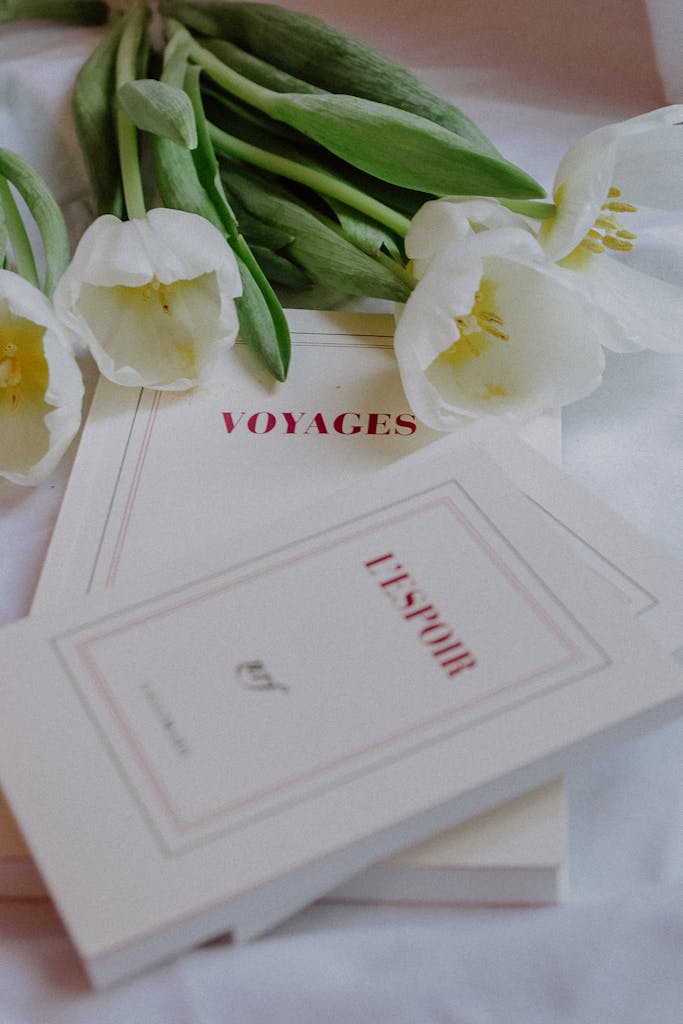 Delicate white tulips paired with French books 'Voyages' and 'L'ESPOIR' in a refined composition.